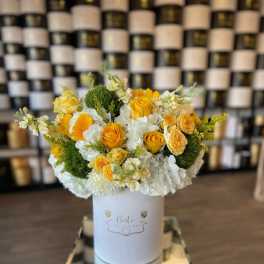 Yellow and white floral arrangement in a white hat box