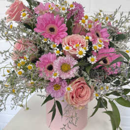 Pink roses and gerbera daisies in a pink hatbox with small white daisies