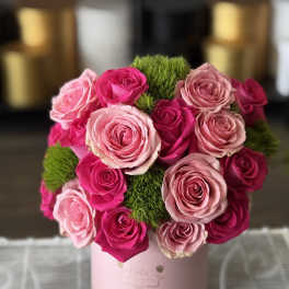 Pink and hot pink roses arranged in a round box with green moss accents