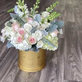 Pink and white roses arranged in a gold round box