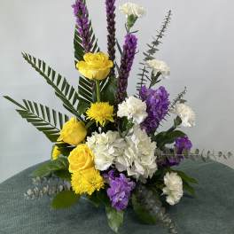 Yellow roses, white carnations, and purple flowers in a tall arrangement