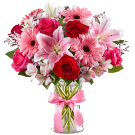Pink and red mixed bouquet in a clear glass vase with a pink ribbon