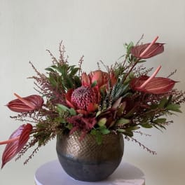 Tropical floral arrangement in a round metallic vase with pink blooms