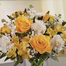 Yellow roses and white flowers arranged in a clear glass vase