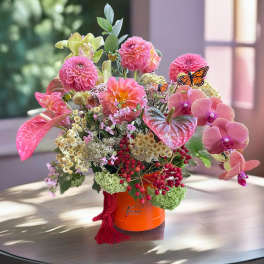Pink and peach floral arrangement in an orange hatbox with butterfly accents
