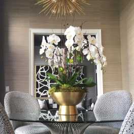 Tall white orchid arrangement in a gold bowl on a table