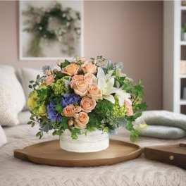 Mixed bouquet of peach roses, white lilies, and blue hydrangeas in a white vase