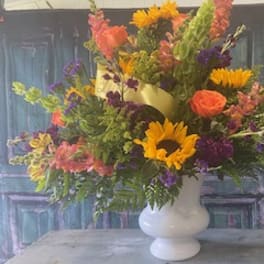 Mixed bouquet in a white vase with sunflowers, roses, and purple blooms