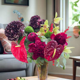 A colorful floral arrangement in a clear vase with purple blooms and red anthuriums.
