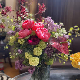 Pink peonies and purple flowers arranged in a glass vase