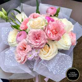 Hand-tied bouquet of pink and cream roses with ranunculus wrapped in white and dotted mesh paper