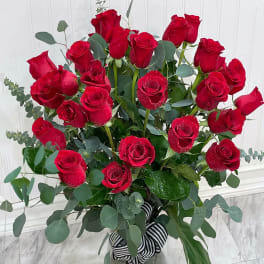 Tall arrangement of long-stemmed red roses in a clear glass vase with striped ribbon