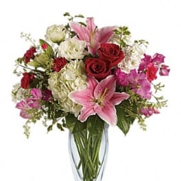 Bouquet of pink lilies, red roses, and white hydrangeas in a clear glass vase