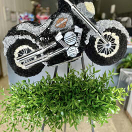 Motorcycle-shaped floral tribute with black, white, and gray flowers on an easel