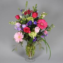Mixed bouquet of pink, purple, and red flowers in a clear glass vase