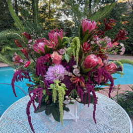 Large pink and purple floral arrangement in a white vase outdoors
