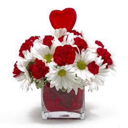 Red carnations and white daisies in a red glass vase with a heart topper