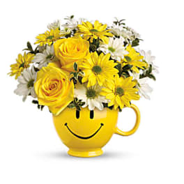 Yellow and white flowers arranged in a smiley-face mug