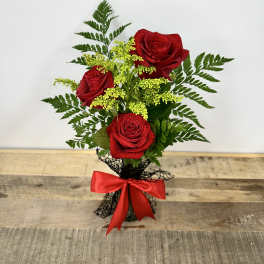 Three red roses with yellow filler in a black wrap and red bow