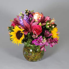 Mixed bouquet with sunflowers, roses, and lilies in a glass vase