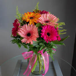 Gerbera daisy bouquet in a glass vase with a pink ribbon