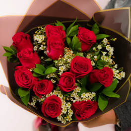 Bouquet of red roses with white filler flowers in dark wrapping