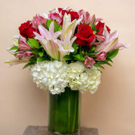 Bouquet of red roses, pink lilies, and white hydrangeas in a glass vase