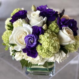 Bouquet of white roses, purple lisianthus, and green hydrangeas in a glass vase
