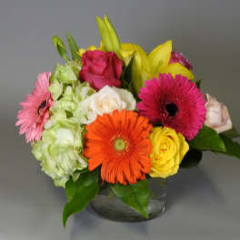 Mixed bouquet of gerbera daisies, roses, lilies, and hydrangea in a glass vase