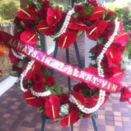 Large red floral standing wreath on an easel with a pink ribbon