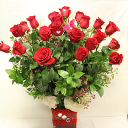 Red roses arranged in a square vase with greenery and white flowers