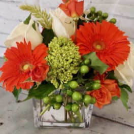 Orange gerbera daisies and white roses in a clear square vase