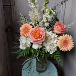 Peach roses and gerbera daisies in a glass vase with white blooms