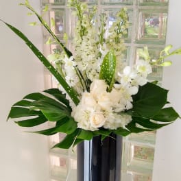 White floral arrangement in a tall black vase with large green leaves