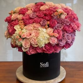 Large round arrangement of pink and lavender roses in a black hat box