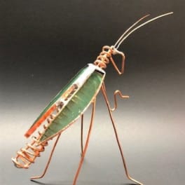 Metal wire grasshopper sculpture with a green body on a dark background