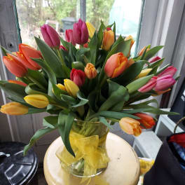 Bouquet of multicolored tulips in a glass vase with a yellow ribbon