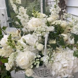 White floral arrangement with roses, hydrangeas, and snapdragons in a basket