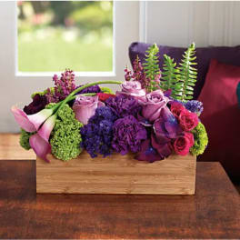 Purple and pink floral arrangement in a wooden box with calla lilies and roses