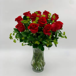 Red roses arranged in a clear glass vase with green filler