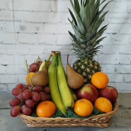Basket of assorted fruit with a pineapple, bananas, grapes, pears, oranges, and apples