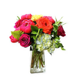 Bright mixed bouquet of pink and orange roses, peonies, and hydrangeas in a clear glass vase