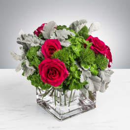 Pink roses in a clear square vase with green and silver foliage