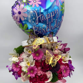 Birthday balloon above a pink and purple flower arrangement in a white box