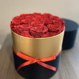 Red roses arranged in a round gold box with a red ribbon