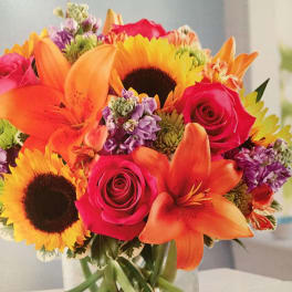 Bright mixed bouquet of sunflowers, roses, and lilies in a glass vase