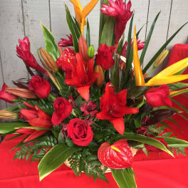 Red floral arrangement with orange tropical blooms and roses in a basket