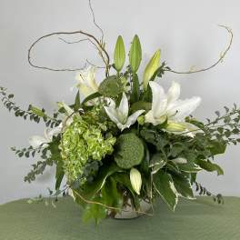 White lilies and green hydrangea in a glass vase with curly branches