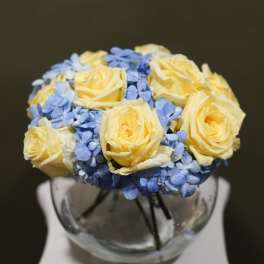 Yellow roses and blue hydrangeas arranged in a glass vase