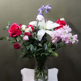 Bouquet of pink roses, white lilies, and lavender flowers in a glass vase